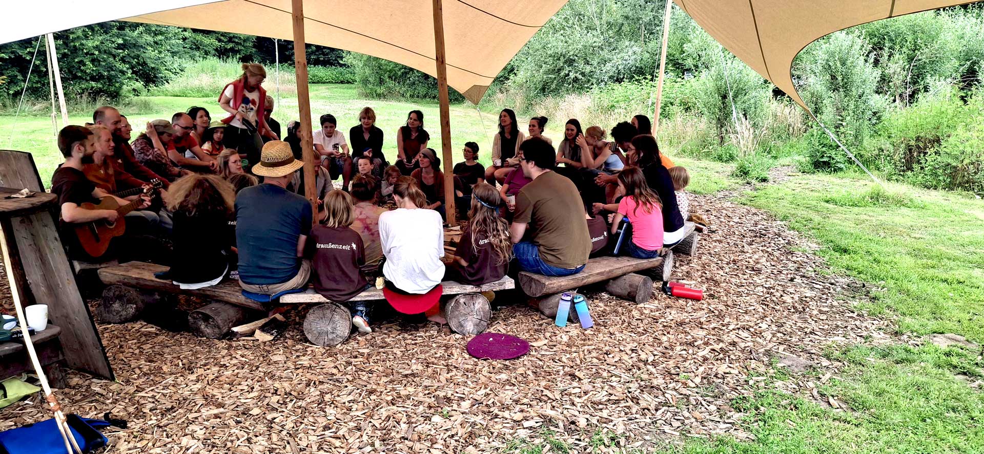 draußenzeit e.V. - Menschen sitzen im Wildniscamp am Feuer und singen